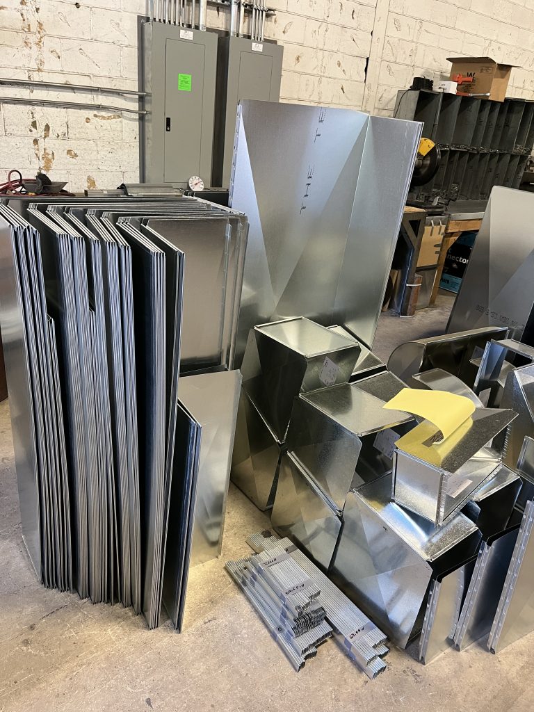 Stacked sheet metal duct panels and fittings in fabrication shop